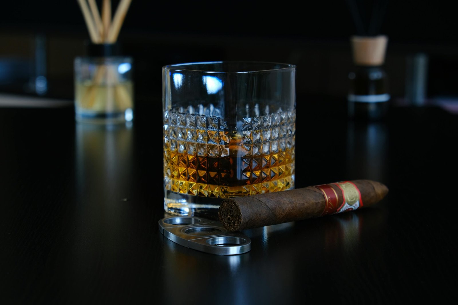 Close-up of a crystal glass with whisky and a cigar on a dark table setting.